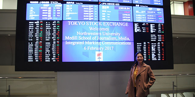 Student standing in front of the Tokyo Stock Exchange digital board.